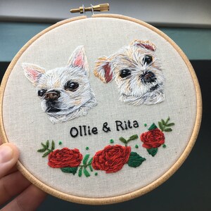 May include: Embroidered portrait of two dogs, a white chihuahua and a brown and white terrier, with the names "Ollie & Rita" stitched below. The portrait is surrounded by a wreath of green leaves and red roses.