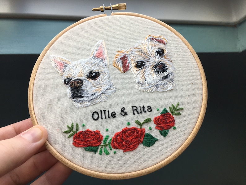 May include: Embroidered portrait of two dogs, a white chihuahua and a brown and white terrier, with the names "Ollie & Rita" stitched below. The portrait is surrounded by a wreath of green leaves and red roses.