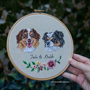 May include: Embroidered portrait of two dogs, Tesla and Khalifa, with a floral design below their names. The embroidery is framed in a wooden hoop.