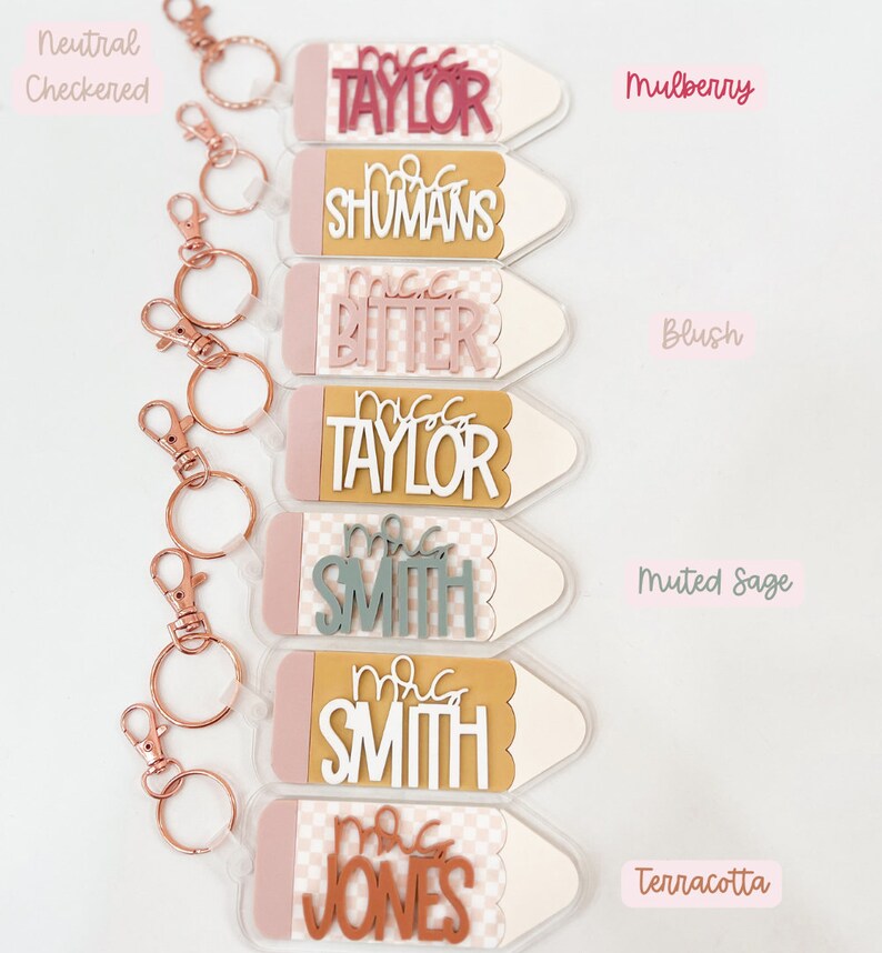 May include: Set of six teacher keychain charms shaped like pencils with different colored backgrounds and names. The names are "Mrs. Taylor", "Mrs. Shumans", "Mrs. Bitter", "Mrs. Taylor", "Mrs. Smith", and "Mrs. Jones".