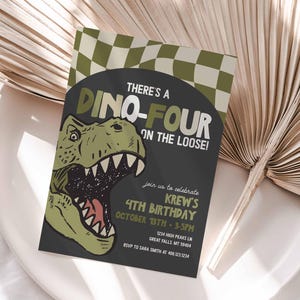 Op de afbeelding: Een verjaardagskaart met een dinosaurus thema. De kaart toont een groene dinosauruskop en de tekst "THERE'S A DINO-FOUR ON THE LOOSE!". De uitnodiging bevat de feestgegevens: datum, tijd en locatie. De uitnodiging ligt op een wit bord.