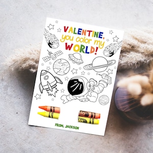 May include: A black and white coloring page with an astronaut, a rocket ship, planets, and stars. The text on the page reads "Valentine, you color my world!" and "From, Jackson".