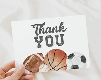 May include: Thank You card with a watercolor illustration of a basketball, football, soccer ball, and baseball. The card is white with black text.