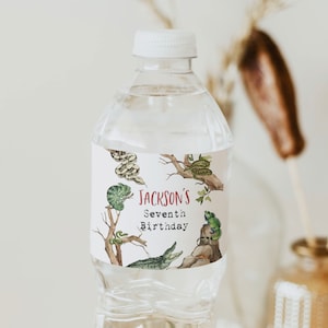 Puede incluir: Una botella de agua de plástico transparente con una etiqueta blanca. La etiqueta tiene una ilustración de acuarela de un camaleón, una serpiente, un caimán y otros animales de la selva. El texto de la etiqueta dice "Jackson's Seventh Birthday".