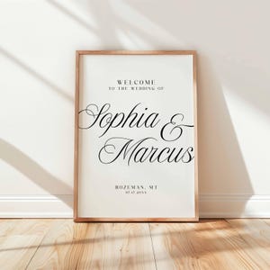 Pu&ograve; includere: Un cartello di benvenuto per matrimoni incorniciato con i nomi "Sophia & Marcus" in elegante corsivo. Il cartello include la localit&agrave;, Bozeman, MT, e la data, 07.17.20XX. La cornice &egrave; marrone chiaro e lo sfondo &egrave; bianco sporco.
