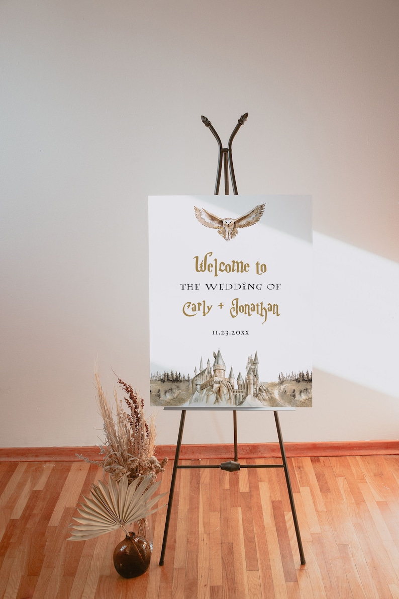 Puede incluir: Un cartel de boda blanco con una ilustraci&oacute;n de acuarela del castillo de Hogwarts y un b&uacute;ho dorado volando por encima. El texto dice "Bienvenido a la boda de Carly + Jonathan 11.23.20XX".