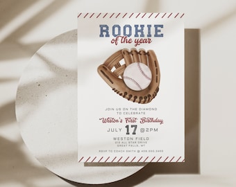 May include: Baseball-themed first birthday party invitation with a red, white, and blue color scheme. The invitation features a cartoon illustration of a baseball glove catching a baseball. The text reads "Rookie of the year" and includes the date and time of the party, the location, and RSVP information.