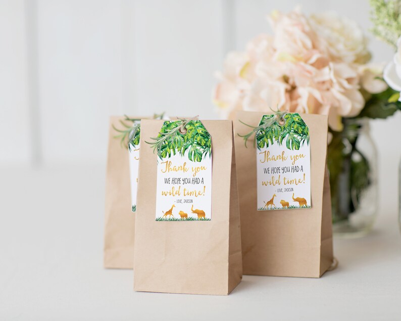 Pode incluir: Sacos de presente de papel kraft com etiquetas com tema de selva. As etiquetas apresentam um design de folha tropical, o texto "Thank you, we hope you had a wild time!" e silhuetas de uma girafa, le&atilde;o e elefante. Um ramo de vegeta&ccedil;&atilde;o est&aacute; anexado.