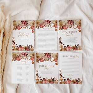May include: A set of six baby shower game cards with floral and apple illustrations. The cards include games like "Baby Sock Hunt," "Dad Jokes," and "My Water Broke." The cards have a warm color palette of cream, brown, and burgundy.