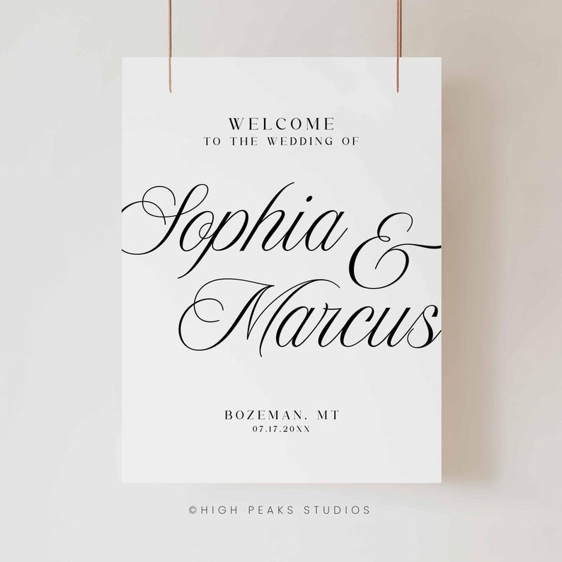 Pu&ograve; includere: Un cartello di benvenuto per matrimoni bianco con scritte nere. Il cartello recita "WELCOME TO THE WEDDING OF Sophia & Marcus" con la localit&agrave; e la data sottostanti. Il cartello &egrave; sospeso da due sottili fili color rame.