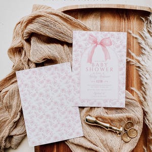May include: A pink and white baby shower invitation with a pink bow and the text "Baby Shower for Ashley Anderson Feb 12th 2 PM The Anderson Residence RSVP to Sarah 555-555-5555 High Peaks Studios LLC"