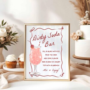 May include: A framed sign with the words "Dirty Soda Bar" in red script. The sign includes instructions for making a soda, and a watercolor illustration of a pink drink with a cherry garnish. The frame is gold.
