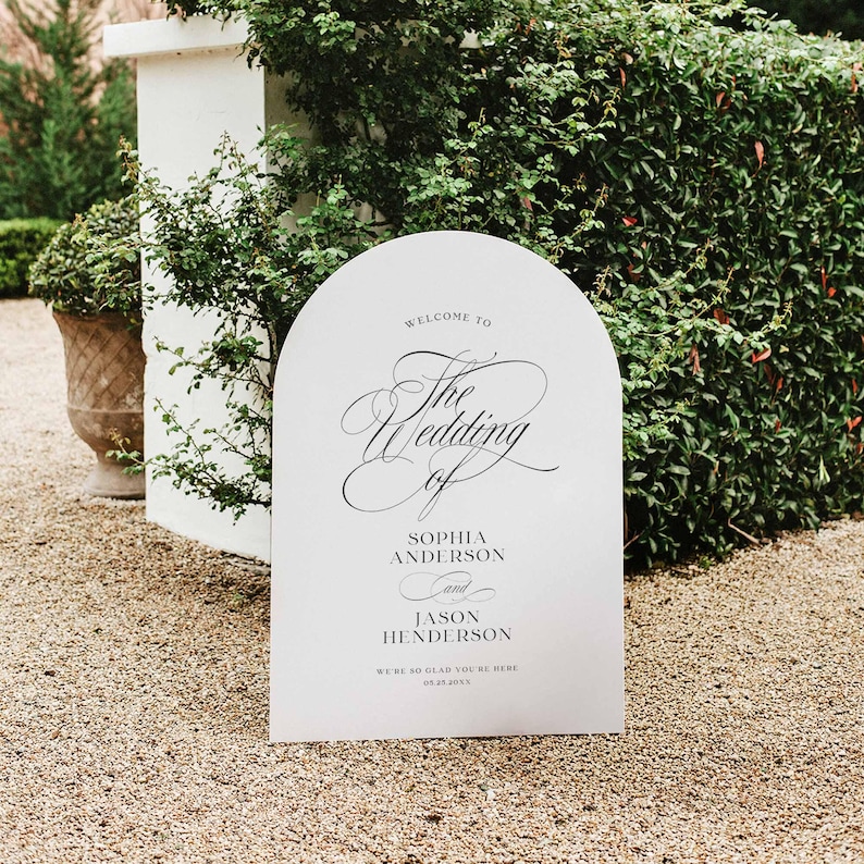 May include: An arched white wedding welcome sign with black text that reads: Welcome to The Wedding of Sophia Anderson and Jason Henderson, we're so glad you're here, 03.25.20XX. The sign features elegant script and serif typography.