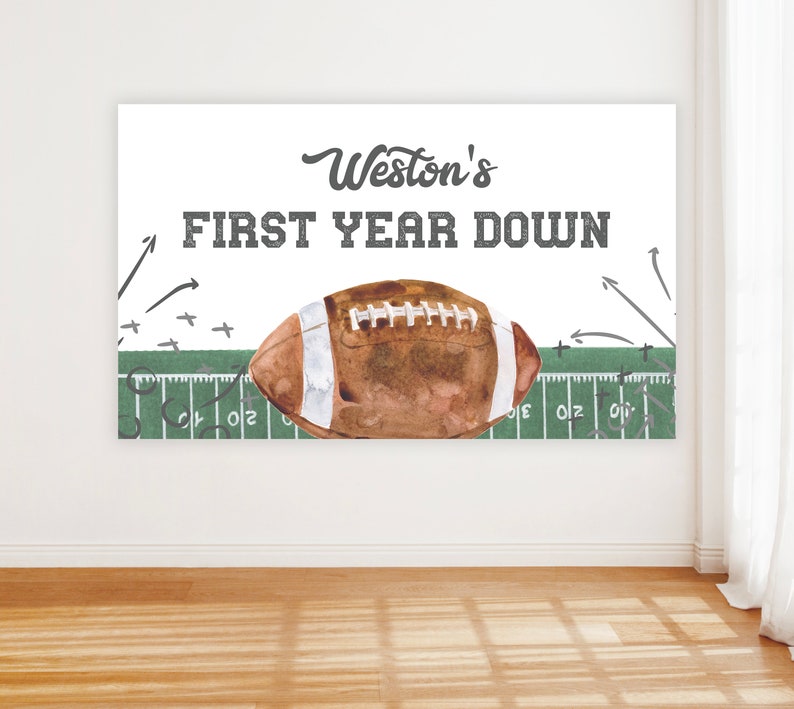 May include: A white banner with green and white football field graphics. The banner says "Weston's First Year Down" with a brown and white football in the center.
