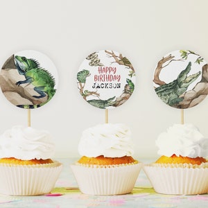 May include: Three round cupcake toppers with a jungle theme. The toppers feature a green iguana, a crocodile, and the text "Happy Birthday Jackson".