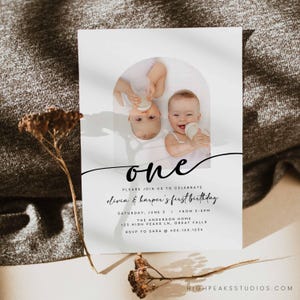以下が含まれることがあります： エレガントな筆記体で「one」と書かれた白い招待状。2人の赤ちゃんが写っており、1人は逆さまに哺乳瓶を持っています。「Olivia & Harper's first birthday」というテキストとイベントの詳細が記載されています。