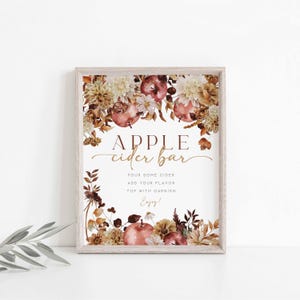 K&ouml;nnte beinhalten: Ein gerahmtes Schild mit den Worten "APPLE cider bar" in eleganter Schrift. Das Schild ist mit Aquarellillustrationen von &Auml;pfeln, Blumen und Bl&auml;ttern in Braun-, Creme- und Burgundert&ouml;nen verziert. Der Text darunter lautet: "Gie&szlig;en Sie etwas Apfelwein ein, f&uuml;gen Sie Ihr Aroma hinzu, garnieren Sie es, genie&szlig;en Sie es!"
