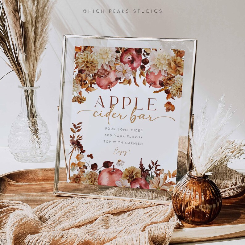 K&ouml;nnte beinhalten: Ein gerahmtes Schild mit dem Text "APPLE cider bar" und floralen und Apfel-Illustrationen. Das Schild enth&auml;lt Anweisungen: "POUR SOME CIDER, ADD YOUR FLAVOR, TOP WITH GARNISH, Enjoy!" Dekorative Elemente sind Vasen mit getrockneten Pflanzen.