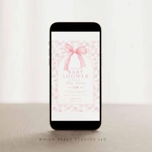 May include: A pink and white baby shower invitation on a smartphone screen. The invitation features a pink bow and a floral pattern. The text reads "Baby Shower" in honor of "Ashley Anderson" on "Feb 12th 3PM".