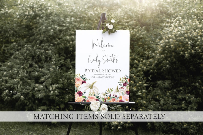 Op de afbeelding: Een wit bord op een zwart schildersezel, met de tekst "Welkom bij Carly Smith's Bridal Shower". Het bord heeft bloemen- en pompoenontwerpen. De datum is 26 september 2021. Het bord staat tegen een achtergrond van groen gebladerte.