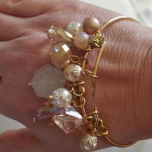 May include: A gold bangle bracelet with a charm chain featuring a variety of pastel-colored beads, including clear, white, and pink. The charms include a flower, a crystal, and a star.