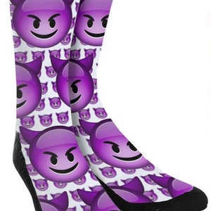 May include: Purple and white socks with a pattern of devil emoji faces. The socks are crew length and have a black toe and heel.