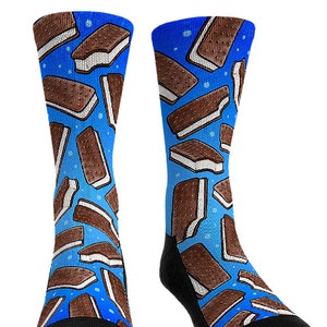 May include: A pair of blue socks featuring a repeating pattern of ice cream sandwiches. The socks have a black heel and toe, and the ice cream sandwiches are brown with white filling. The background is a light blue with small white dots.