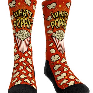 May include: Novelty socks with a red background and a popcorn theme. The socks feature the words "WHAT'S POPPIN" in yellow, along with popcorn kernels and a popcorn box design. The toe and heel are black.