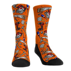 May include: A pair of orange socks with a pattern of various tools, including a saw, hammer, screwdriver, drill, and nails.