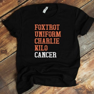 May include: Black t-shirt with the words "FOXTROT UNIFORM CHARLIE KILO CANCER" printed in orange and white.