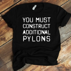 May include: Black t-shirt with white text that reads "YOU MUST CONSTRUCT ADDITIONAL PYLONS".