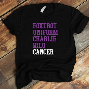 May include: Black t-shirt with the words "FOXTROT UNIFORM CHARLIE KILO CANCER" in purple and white lettering.