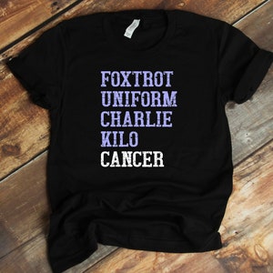 May include: Black t-shirt with the words "FOXTROT UNIFORM CHARLIE KILO CANCER" printed in white with a purple outline.