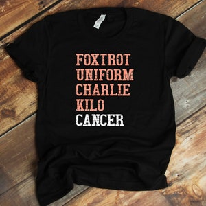 May include: Black t-shirt with the words "FOXTROT UNIFORM CHARLIE KILO CANCER" printed in pink on the front.