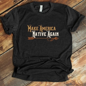 May include: Dark gray t-shirt with the text "Make America Native Again" in brown and white lettering. An arrow with feathers is below the text.