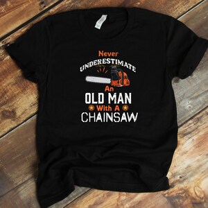 May include: Black t-shirt with a white graphic that says "Never underestimate an old man with a chainsaw". The graphic includes a chainsaw and a star.