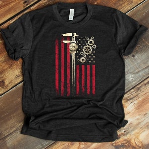 May include: A dark heather grey t-shirt with a graphic of a caliper, gears, and stars in the shape of an American flag.