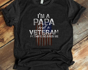 Może przedstawiać: Szary t-shirt z nadrukiem "I'm a Papa and a Veteran Nothing Scares Me". Grafika amerykańskiej flagi znajduje się za tekstem.