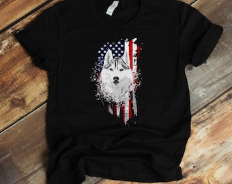 May include: Black t-shirt with a white husky dog head graphic. The dog is in front of a distressed American flag.