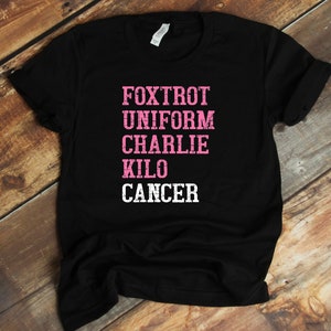 May include: Black t-shirt with the words "FOXTROT UNIFORM CHARLIE KILO CANCER" in pink and white lettering.
