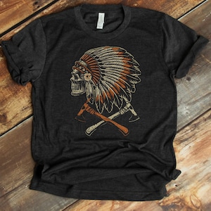 May include: A dark grey t-shirt featuring a graphic print of a skull wearing a Native American headdress and crossed axes.