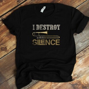 Könnte beinhalten: Schwarzes T-Shirt mit dem Text "I DESTROY SILENCE" über einer goldenen Posaunen-Grafik. Der Text ist in einer Used-Schriftart gehalten, was ihm einen Vintage-Look verleiht. Das Shirt ist aus weichem Material.