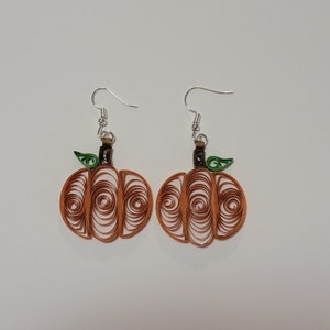 May include: A pair of orange pumpkin-shaped earrings with green leaves and silver hooks. The pumpkins are made of paper and have a spiral design.