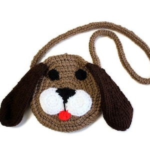 May include: A brown crocheted dog-shaped purse with a white face, black eyes, and a red tongue. The purse has a brown crocheted strap.