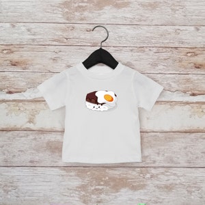 May include: White t-shirt with a cartoon illustration of a plate of rice topped with a fried egg and gravy. The food has a smiling face.