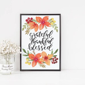 May include: A framed print with a watercolor illustration of fall leaves and flowers in shades of orange, red, and yellow. The print features the text "grateful thankful blessed" in black calligraphy.