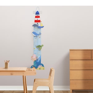 May include: A wooden lighthouse-shaped height chart with a nautical theme. The chart features a red and white striped lighthouse, a sailboat, a whale, a turtle, and an octopus. The chart measures in inches and centimeters, with the name "Lily" at the top.