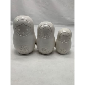 Puede incluir: Tres mu&ntilde;ecas rusas blancas s&oacute;lidas dispuestas en fila de mayor a menor. Cada mu&ntilde;eca presenta un acabado liso y brillante con un rostro moldeado y un dise&ntilde;o floral en relieve &uacute;nico en la parte inferior del cuerpo de cada figura.