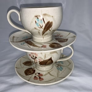 May include: A set of two vintage teacups and saucers with a floral pattern in shades of brown, blue, and pink. The cups and saucers are made of ceramic and have a white background.