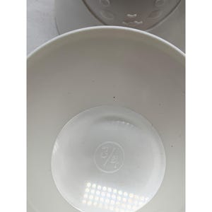 Puede incluir: Una taza medidora de pl&aacute;stico blanco con un interior liso y redondeado. El fondo de la taza presenta una marca de medici&oacute;n en relieve de 3/4 cup, centrada dentro de una hendidura circular en la base del recipiente.